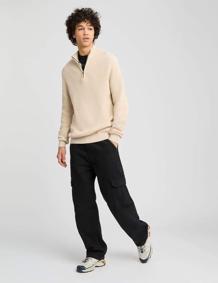 T-shirt noir avec pull col demi-zippé beige sable, pantalon cargo et sneakers trail