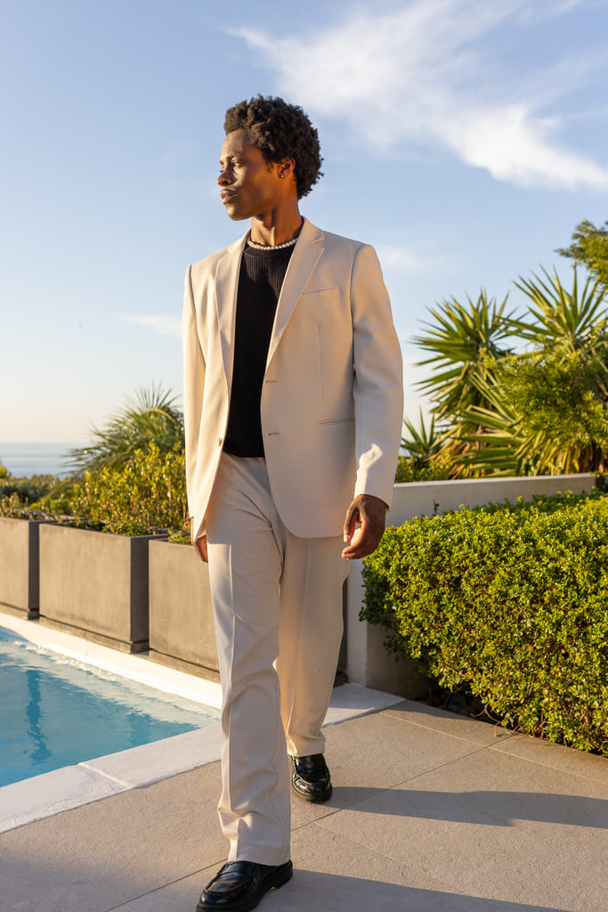 Costume beige crème associé à un t-shirt noir col rond, loafers noirs et collier de perles pour un contraste affirmé