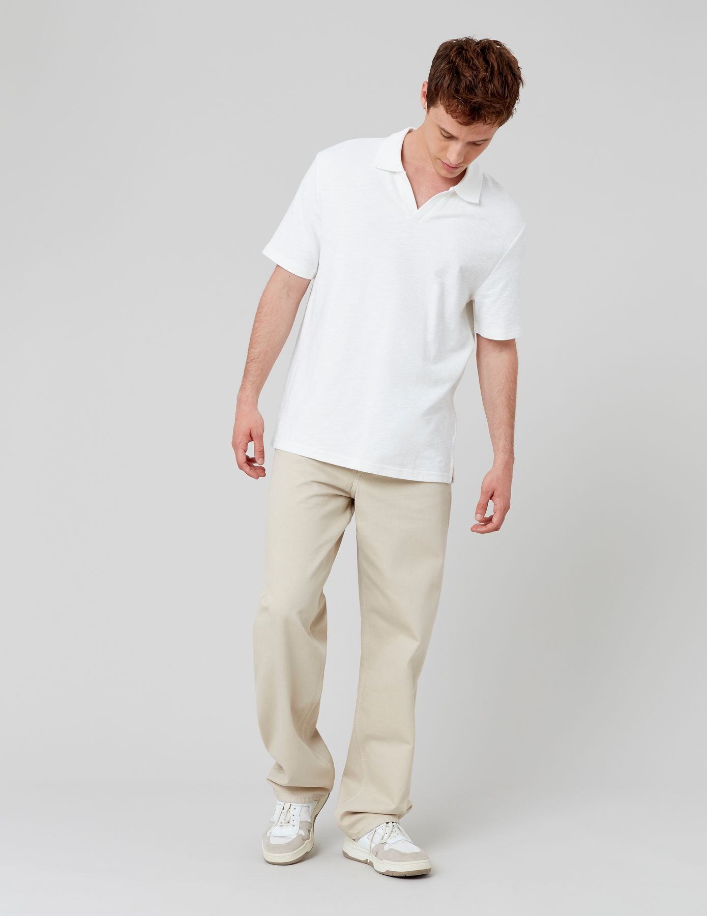 Polo blanc à col ouvert avec pantalon baggy beige sable et sneakers blanches basses