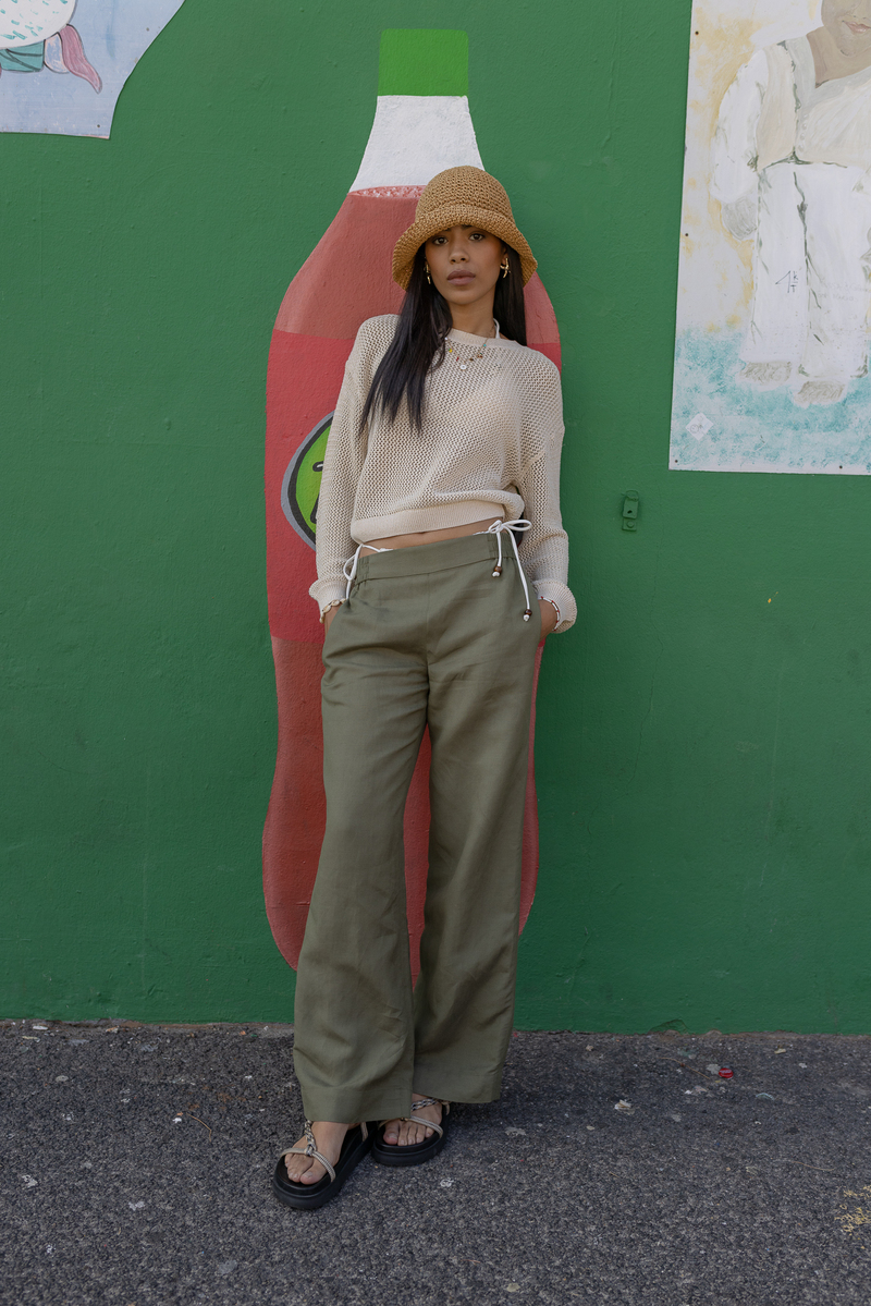Look boho-urbain : pull crochet ajouré en coloris naturel associé à un pantalon large kaki à taille haute avec liens contrastants, bucket hat en raphia tressé et sandales à multi-brides argent