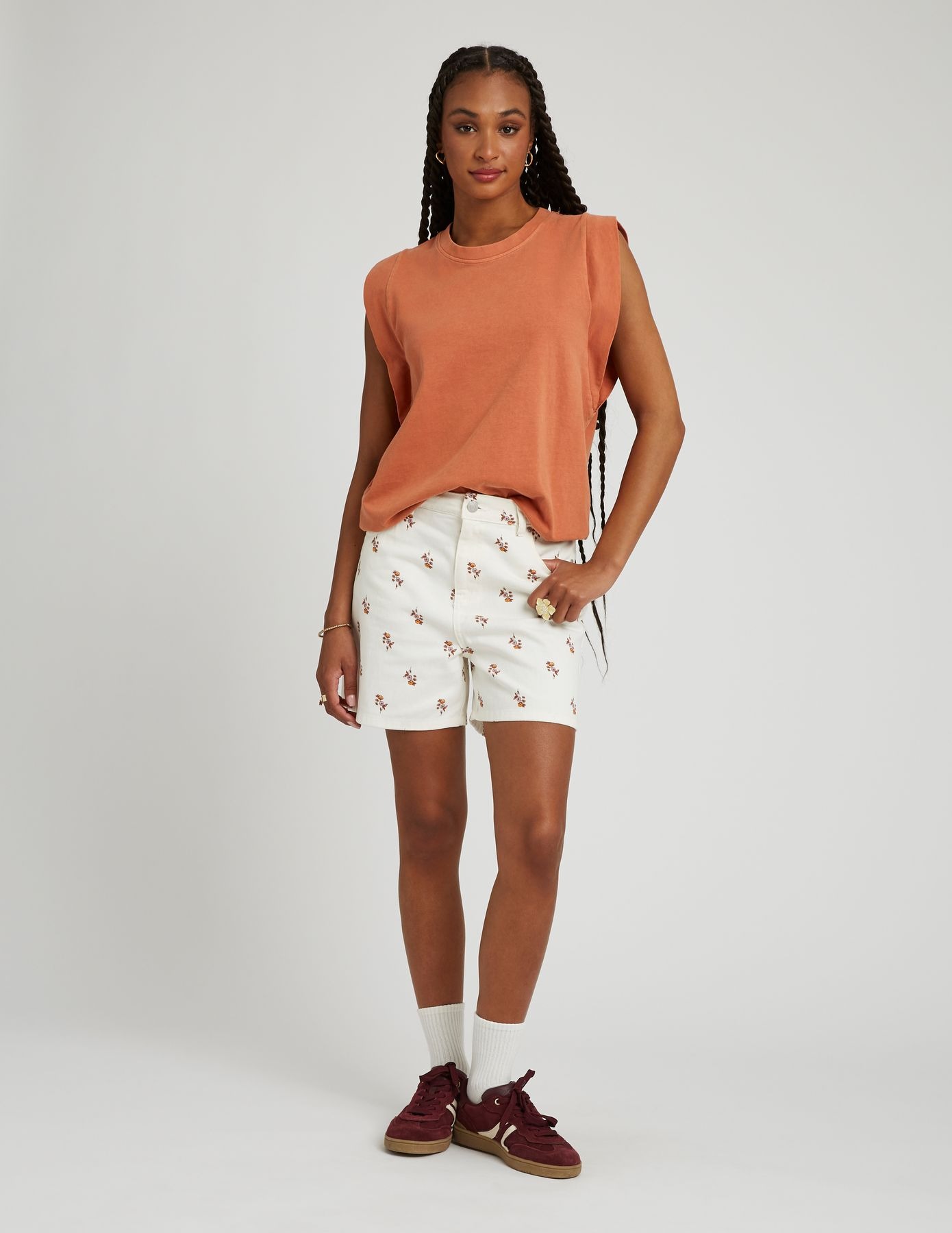 Look femme été avec un short blanc à imprimé fleuri et un top sans manches terracotta, complété par des sneakers bordeaux