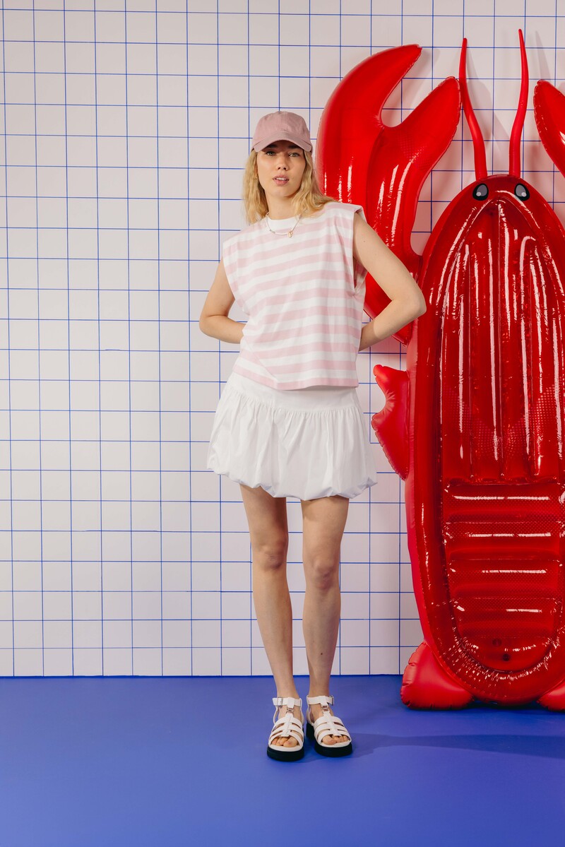 Look bord de mer : marinière crop sans manches à épaulettes rose poudré et blanc associée à une jupe bouffante blanche courte, casquette rose poudrée et sandales blanches à brides