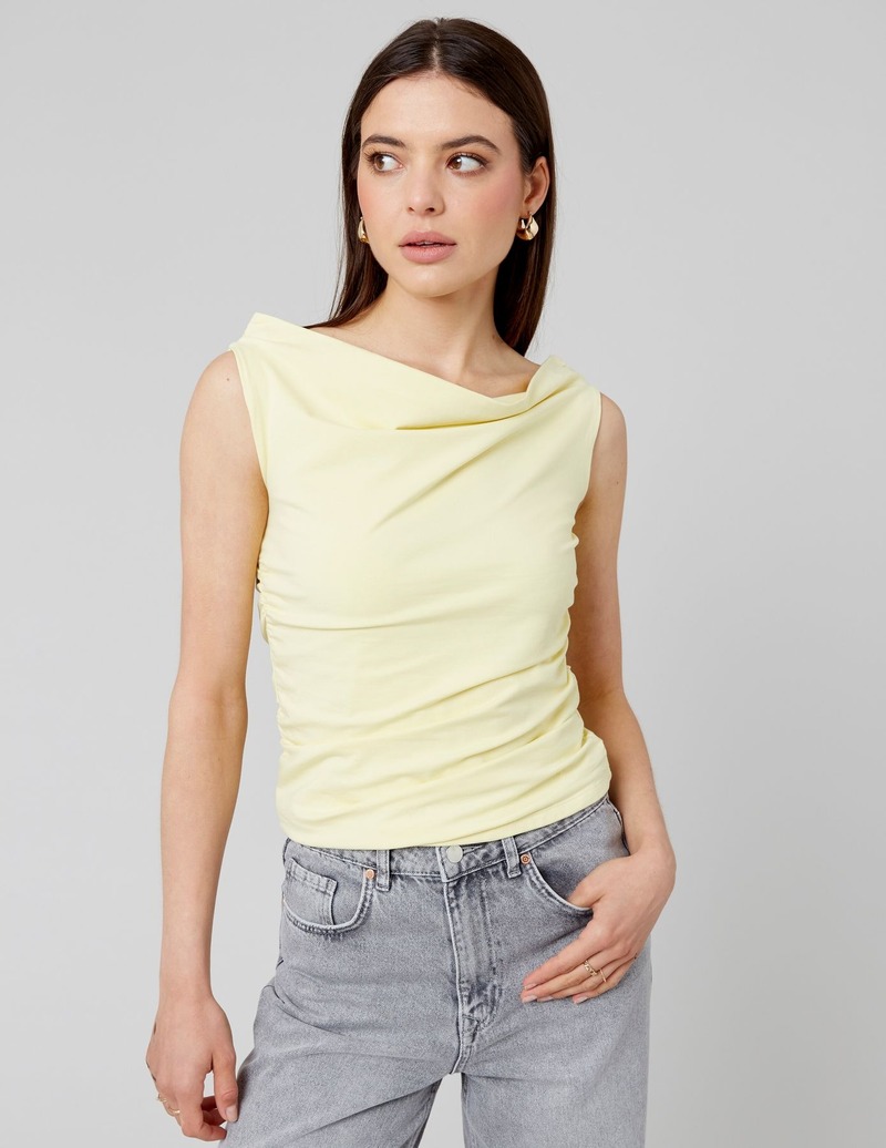 Look élégant sans effort : top sans manches citron doux à col asymétrique drapé et fronces latérales associé à un jean gris, complété par des créoles dorées et bagues fines