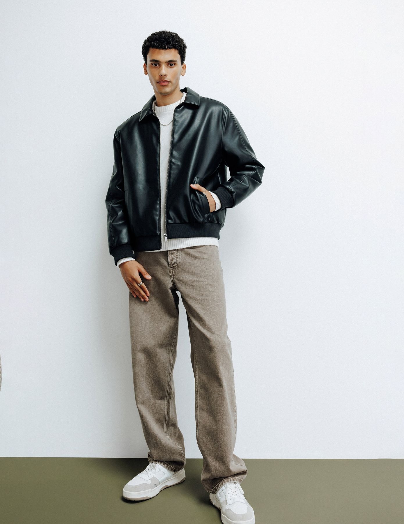 Blouson en simili cuir noir avec pull col roulé blanc et jean baggy taupe, sneakers blanches basses