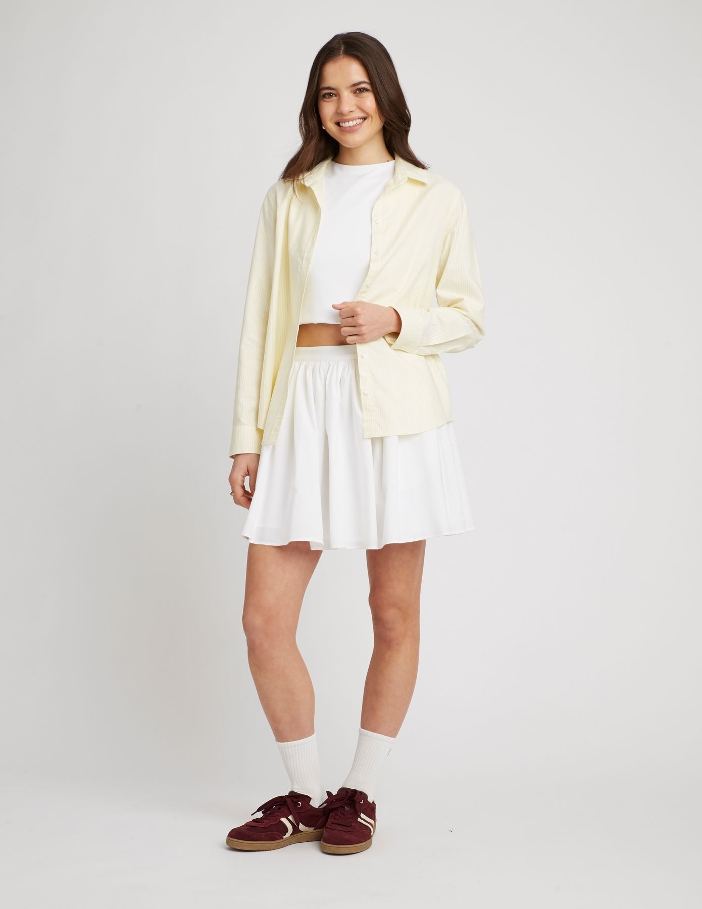 Total look blanc avec t-shirt blanc crop-top, jupe blanche, chemise jaune pastel et baskets bordeaux