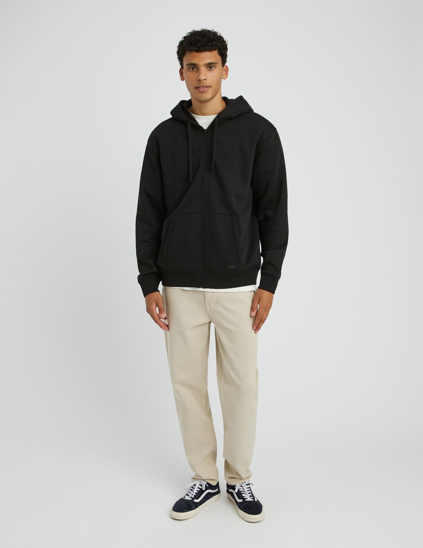 Homme en sweat col polo demi-zip noir avec un jean brut bleu marine et des baskets sombres