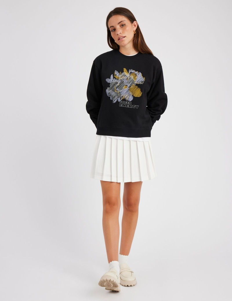 Look sporty-chic : sweat graphique oversize noir avec motif brodé coloré associé à une jupe plissée blanche ultra-courte, chunky shoes crème et chaussettes fantaisie