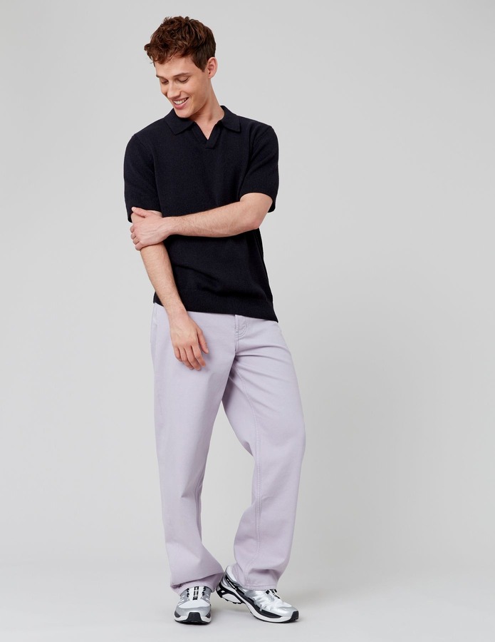 Look streetwear tendance avec polo tricoté noir à col ouvert et pantalon large lilas pastel, sneakers running argentées