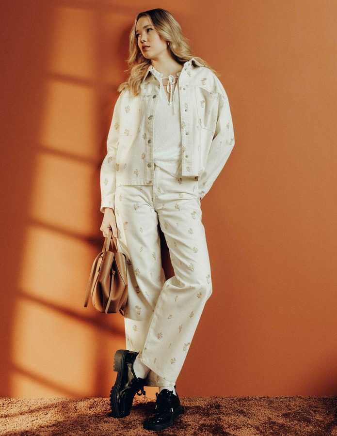 Look boho printanier avec jean wide leg en denim clair brodé de fleurs blanches, t-shirt kaki et veste en broderie anglaise blanche