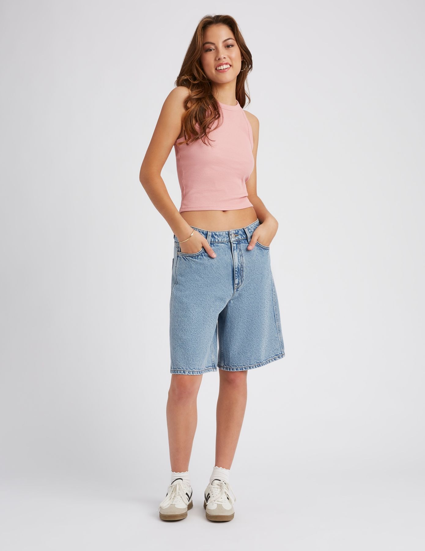 Femme portant un bermuda en jean bleu clair délavé avec un crop top rose et des sneakers blanches