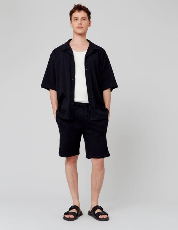 Homme en ensemble coordonné chemise et short noirs gaufrés avec un t-shirt blanc et des sandales