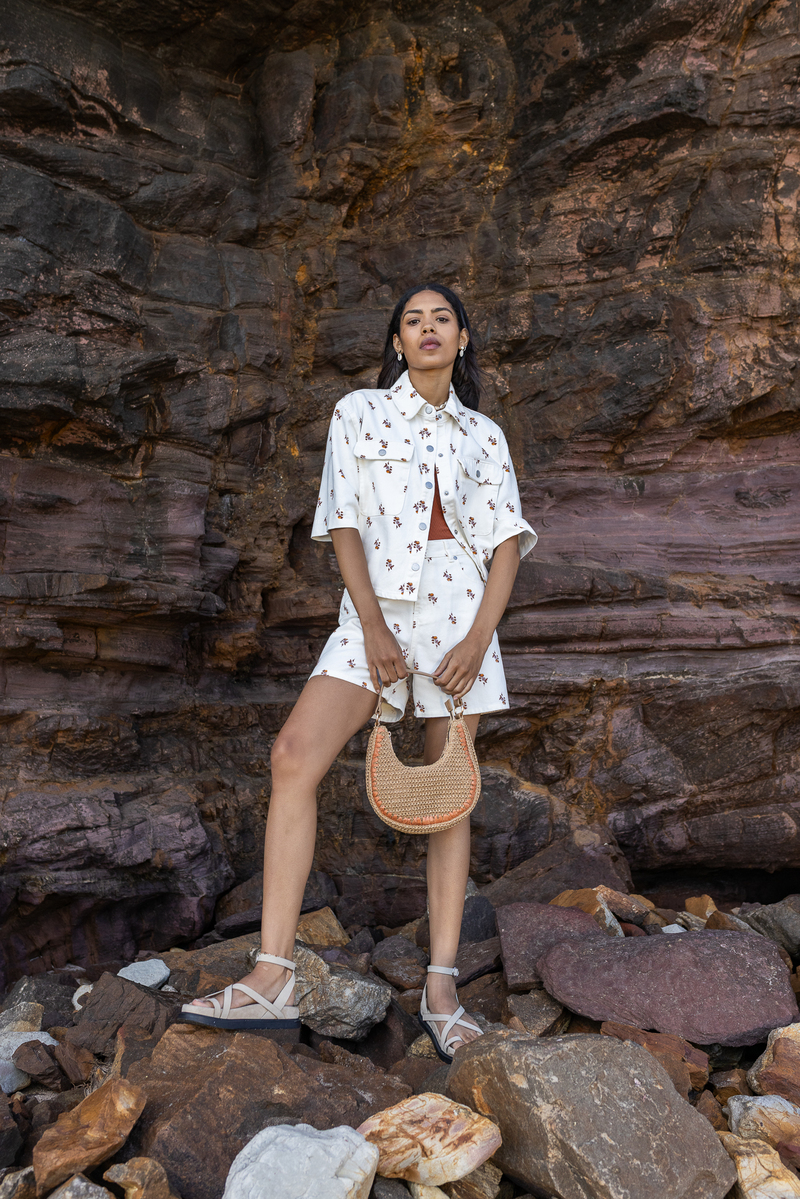 Look co-ord tendance : veste courte boutonnée et short assorti en imprimé fleuri blanc et terracotta, avec top terracotta vif, sac demi-lune en raphia et sandales minimalistes à lanières