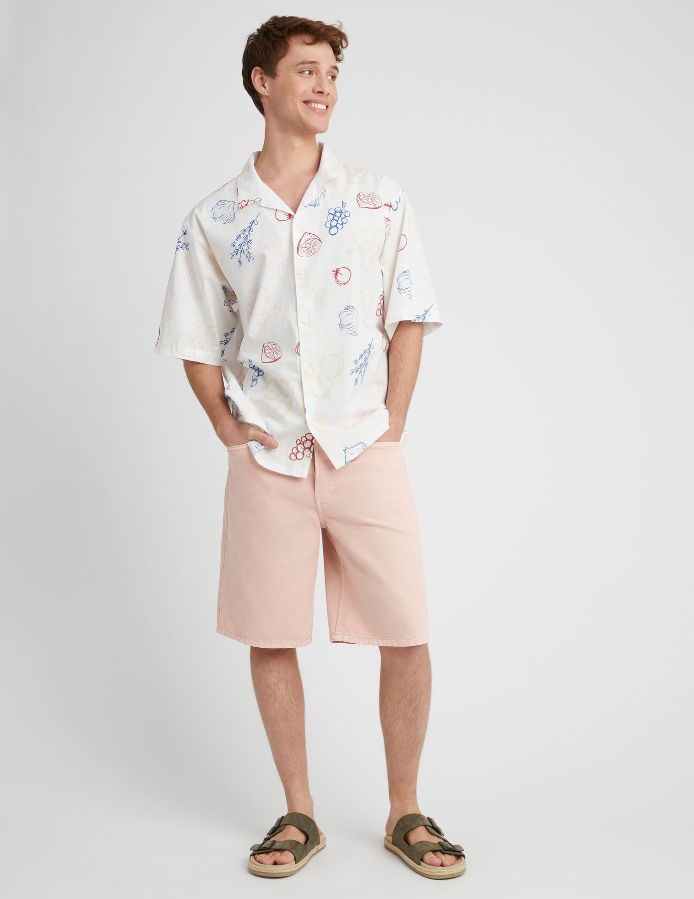 Look vacances estival avec bermuda rose pêche, chemise à motifs et sandales kaki