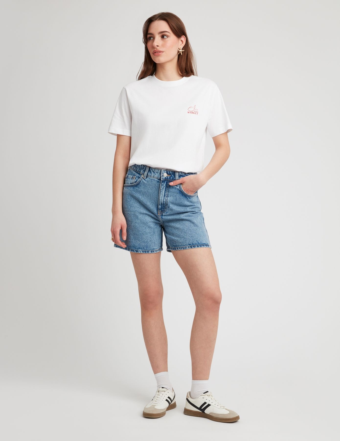 Look femme été avec un short en jean denim bleu à coupe droite associé à un t-shirt blanc oversize graphique et des sneakers rétro blanc et noir