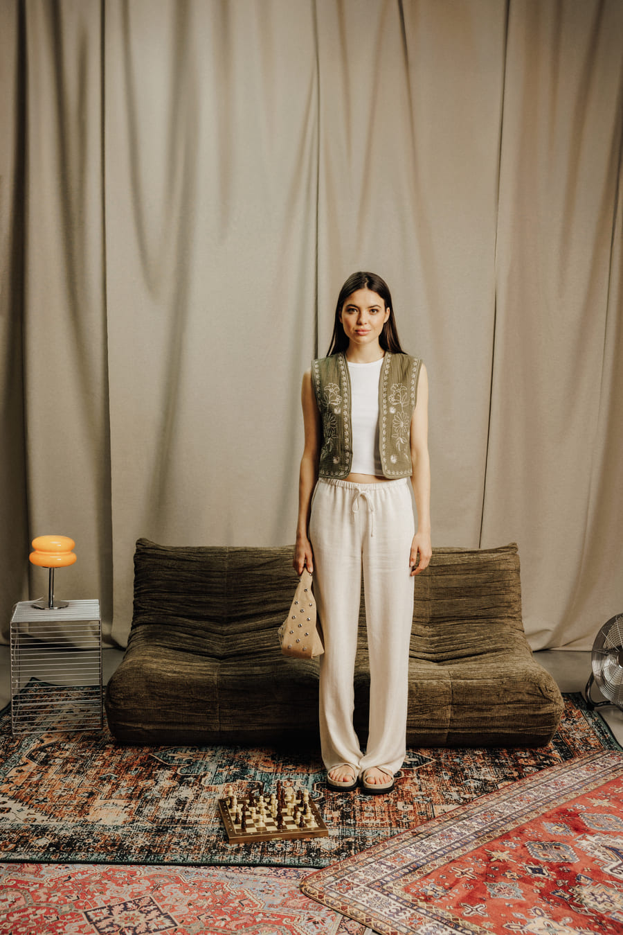 Pantalon large en maille crème avec crop top blanc côtelé et gilet sans manches brodé kaki porté ouvert, sandales plates et mini sac à poignée clouté