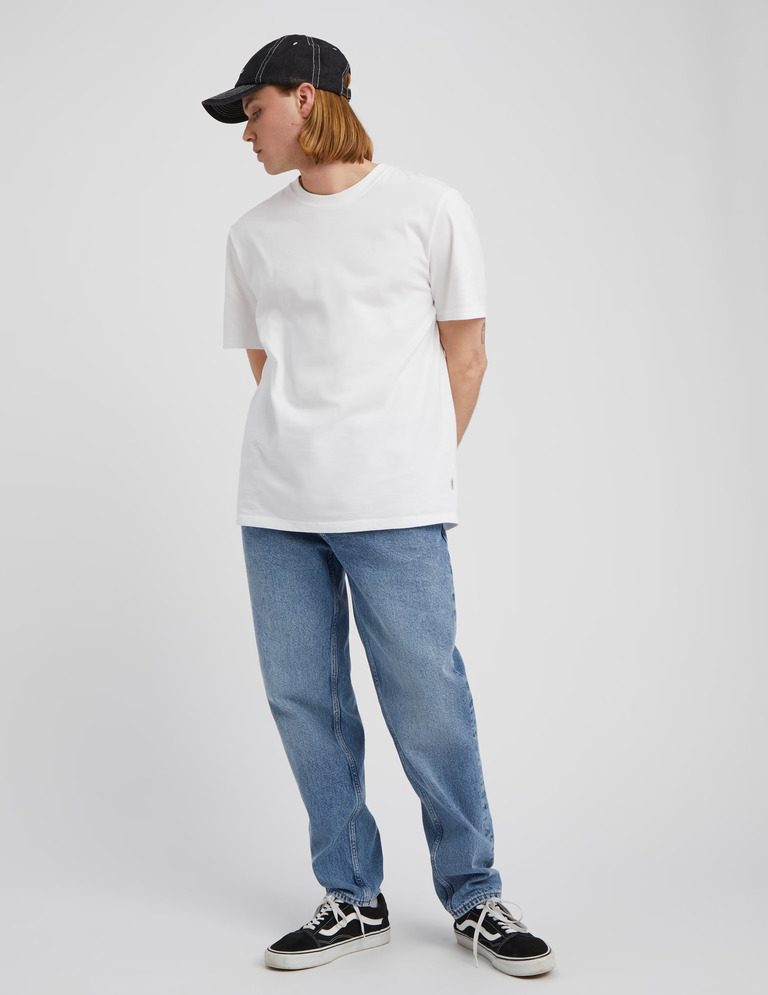 Look homme avec jean loose bleu, t-shirt blanc, casquette noire et sneakers
