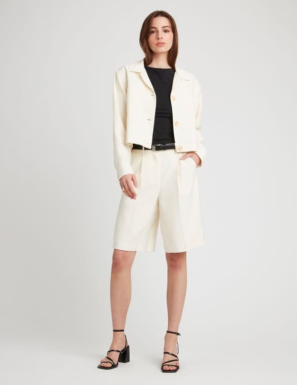 Tenue élégante avec bermuda tailleur beige, top noir, veste blanche et sandales à talons