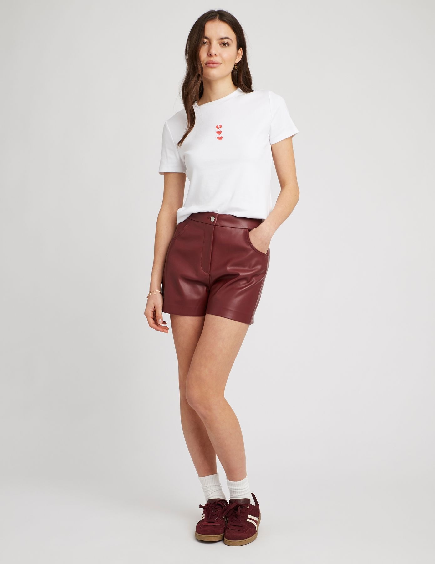 Look femme audacieux avec un short simili cuir bordeaux taille haute associé à un t-shirt blanc à cœurs rouges brodés et des sneakers bordeaux assortis