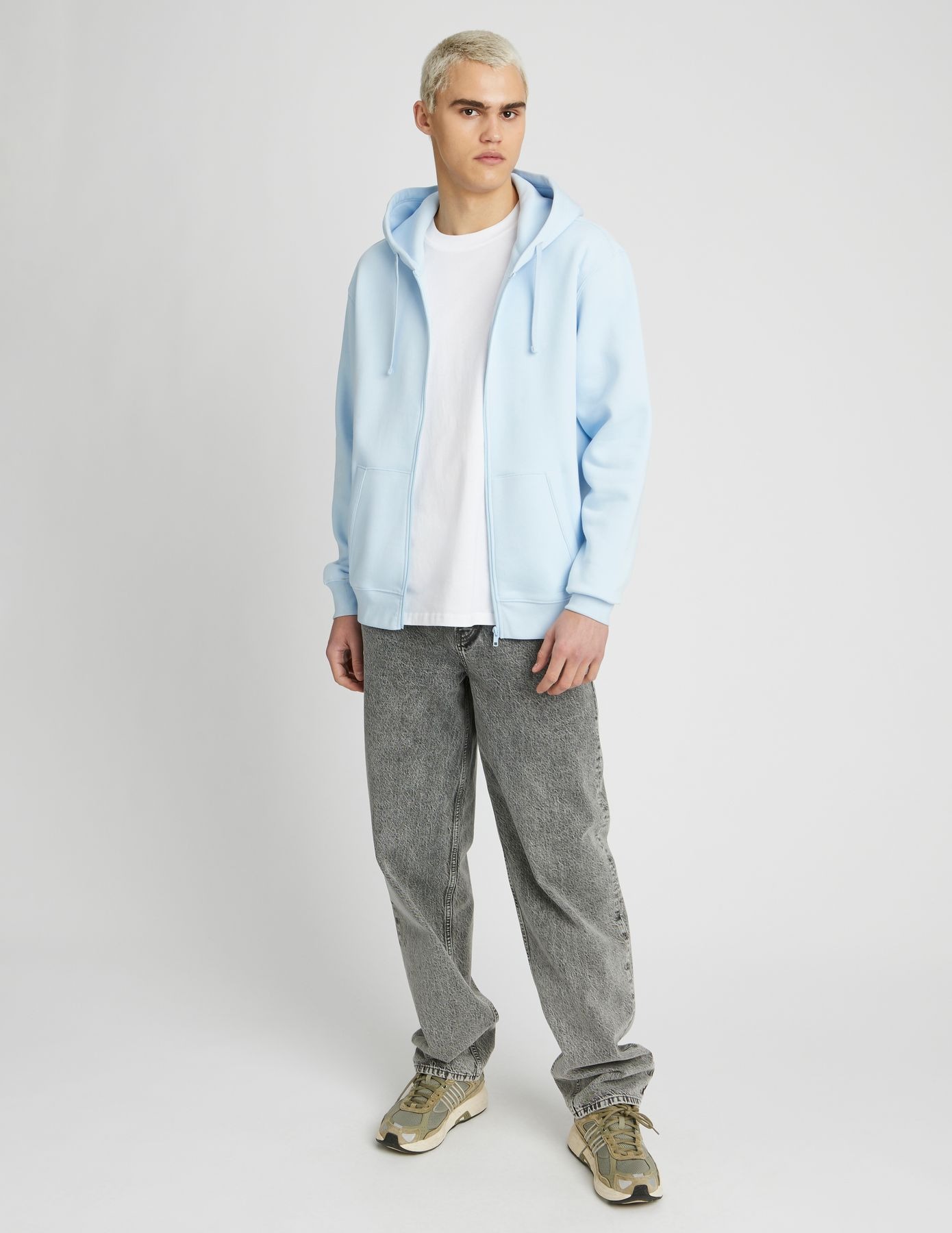 Sweat zippé à capuche bleu ciel pastel ouvert sur t-shirt blanc avec jean baggy gris acide et sneakers kaki