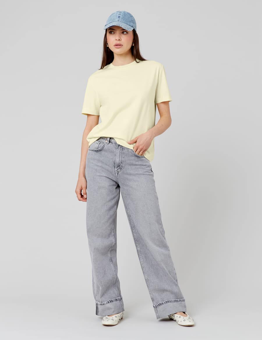 Jean large gris délavé associé à un t-shirt oversize jaune pâle, casquette denim et mules à détails