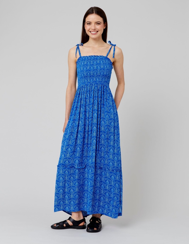 Robe longue à imprimé bleu intense avec bretelles nouées, corsage smocké et jupe ample fluide, portée avec des sandales noires plates à semelles épaisses