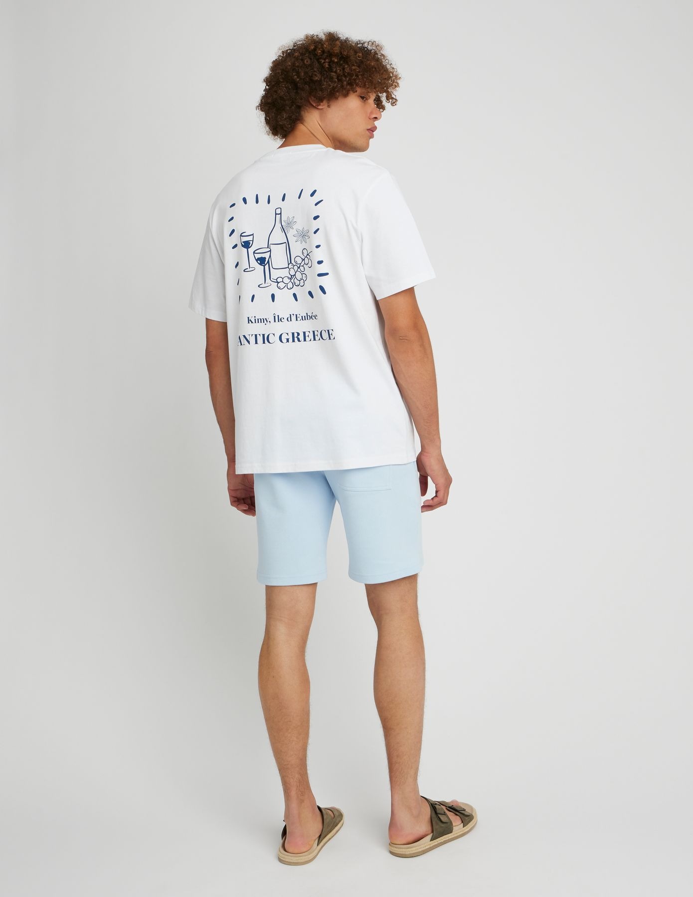 Look minimaliste estival avec bermuda bleu clair, t-shirt blanc graphique et sandales