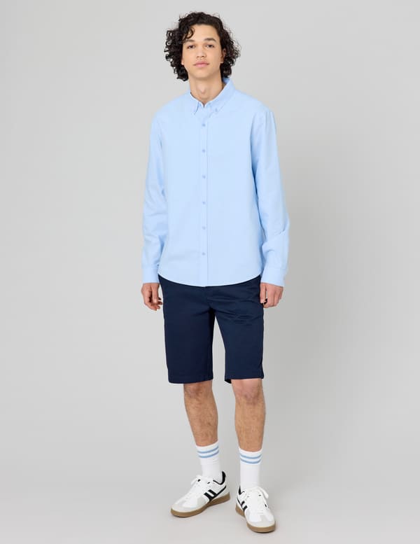 Homme en chemise Oxford bleu ciel et bermuda chino bleu marine avec des sneakers blanches