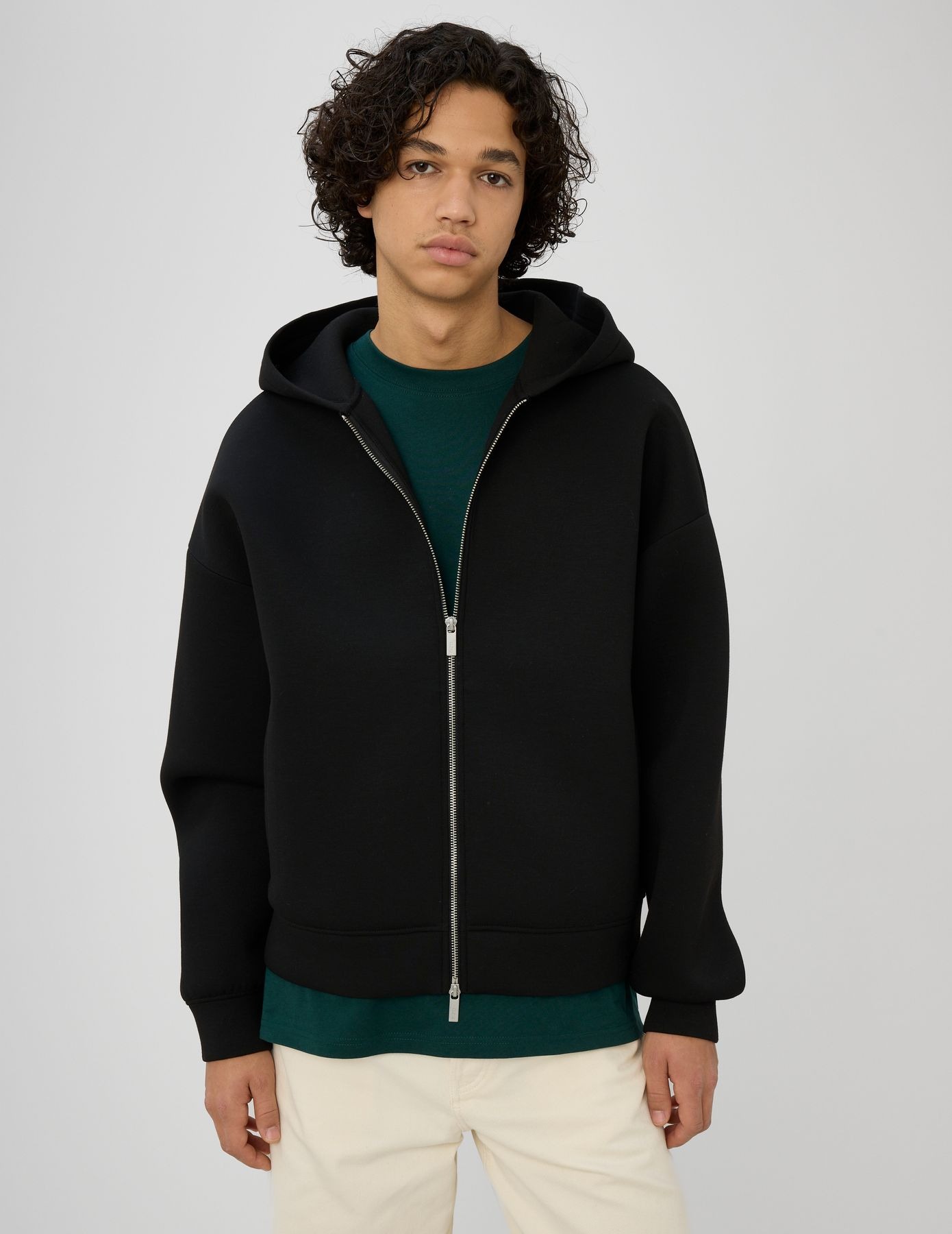 Homme en sweat zippé à capuche noir oversize ouvert sur un t-shirt vert profond avec un jean
