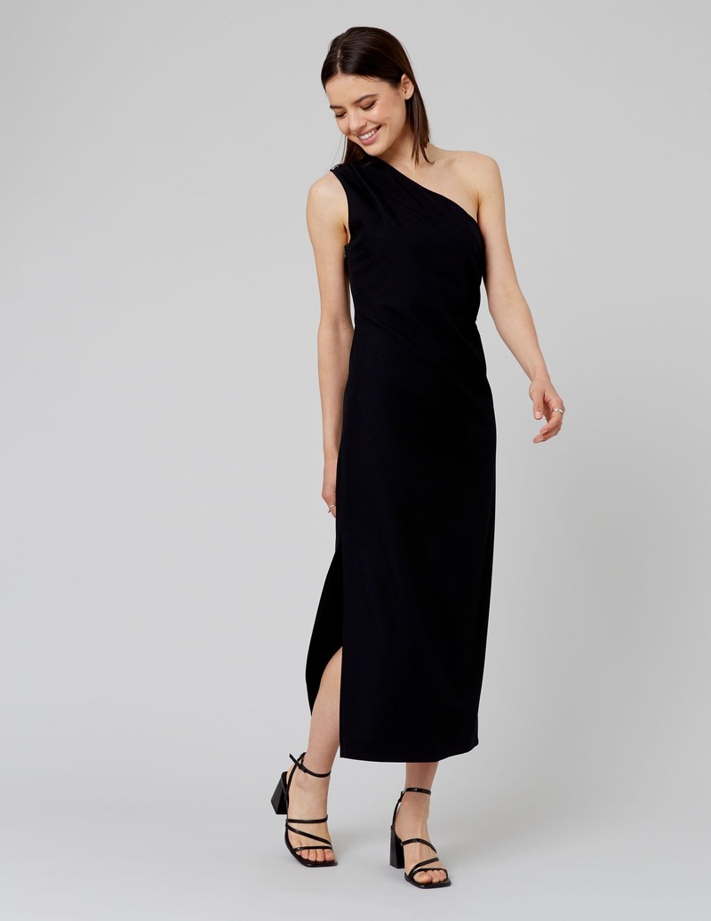 Robe longue noire asymétrique one-shoulder avec fente latérale pour une soirée estivale minimaliste, portée avec des sandales à lanières multiples à talons carrés