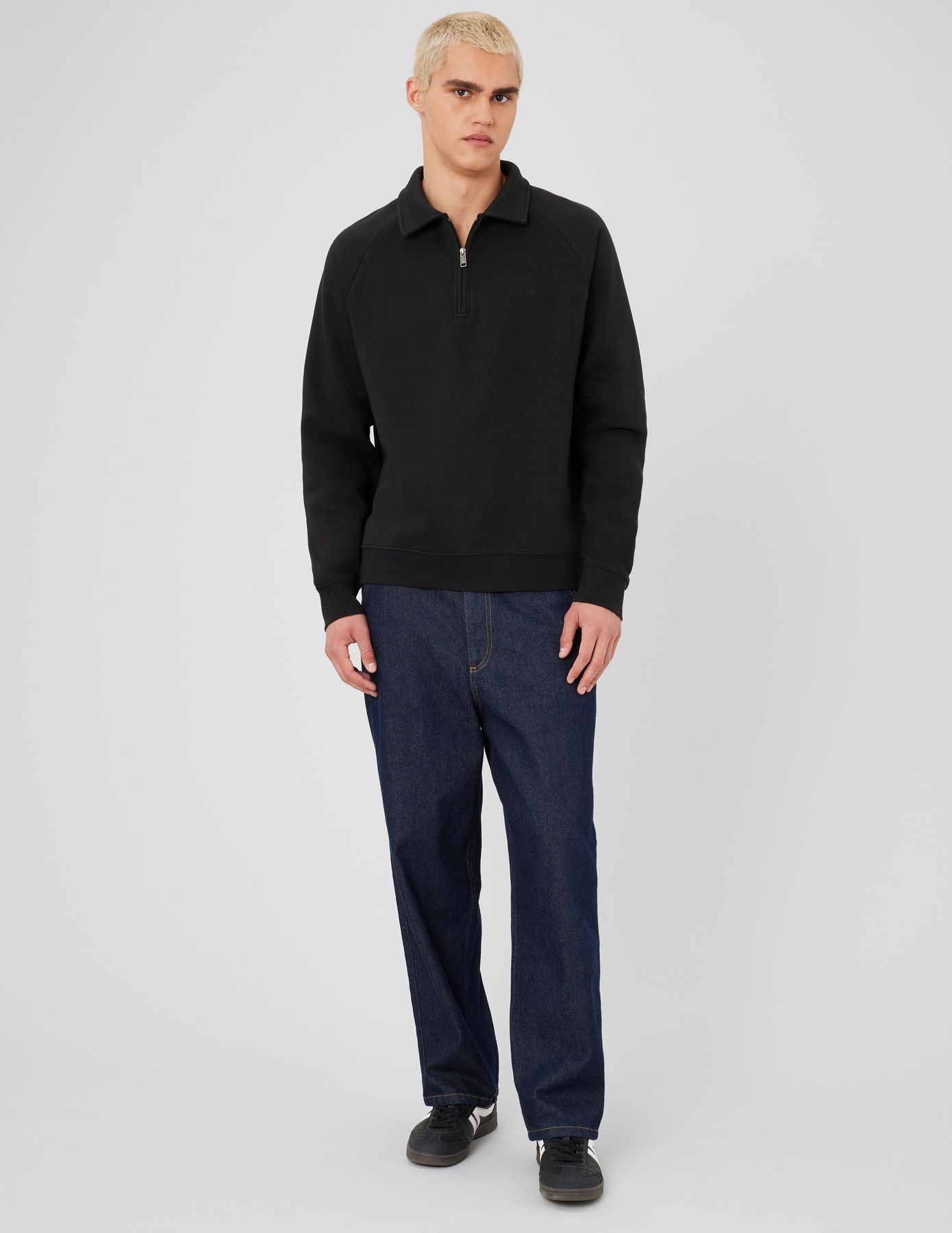 Homme en sweat zippé à capuche noir sur t-shirt blanc avec un pantalon beige et des baskets bleu marine