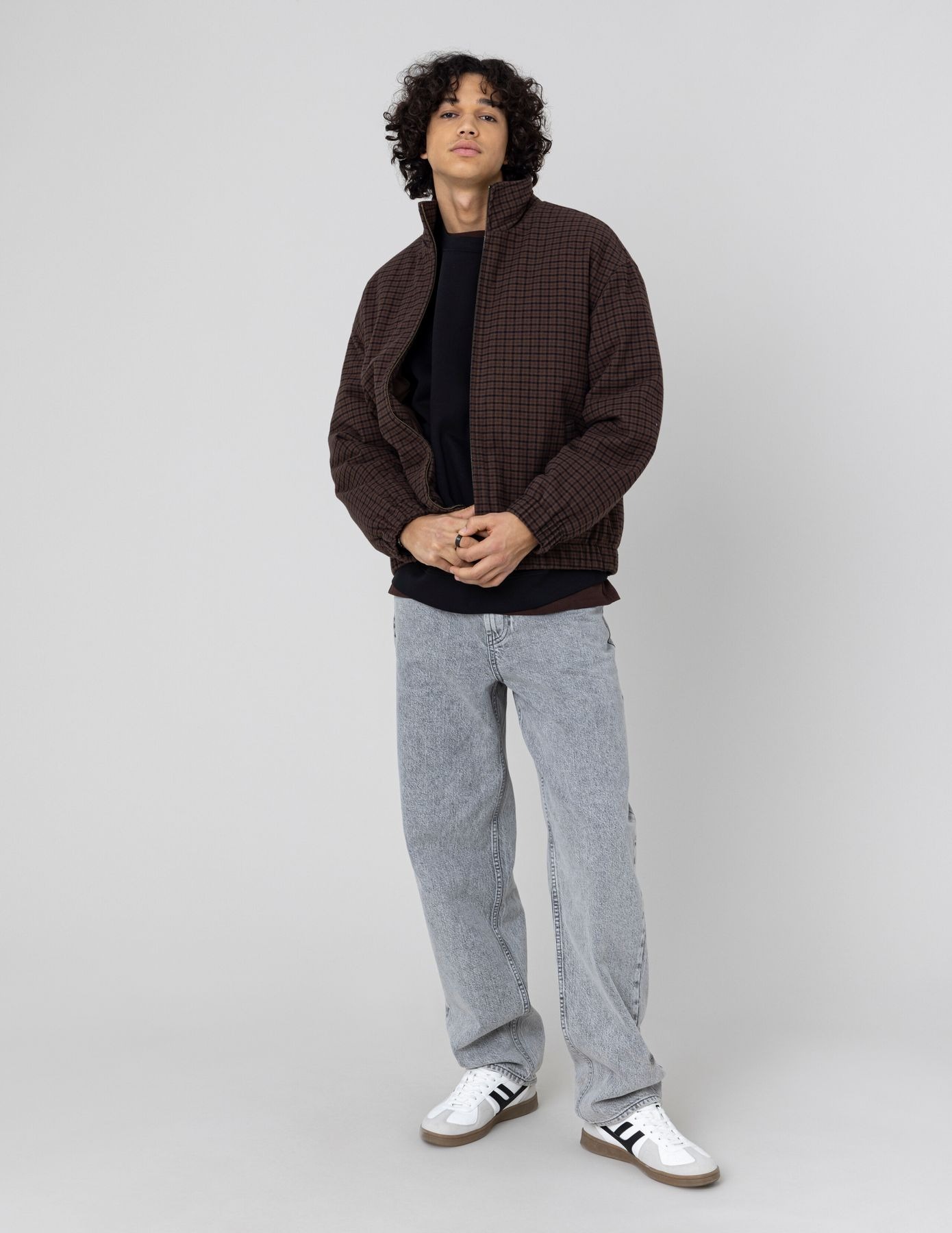 Homme en sweat noir sous une veste à carreaux marron ouverte avec un jean large gris clair et des baskets blanches
