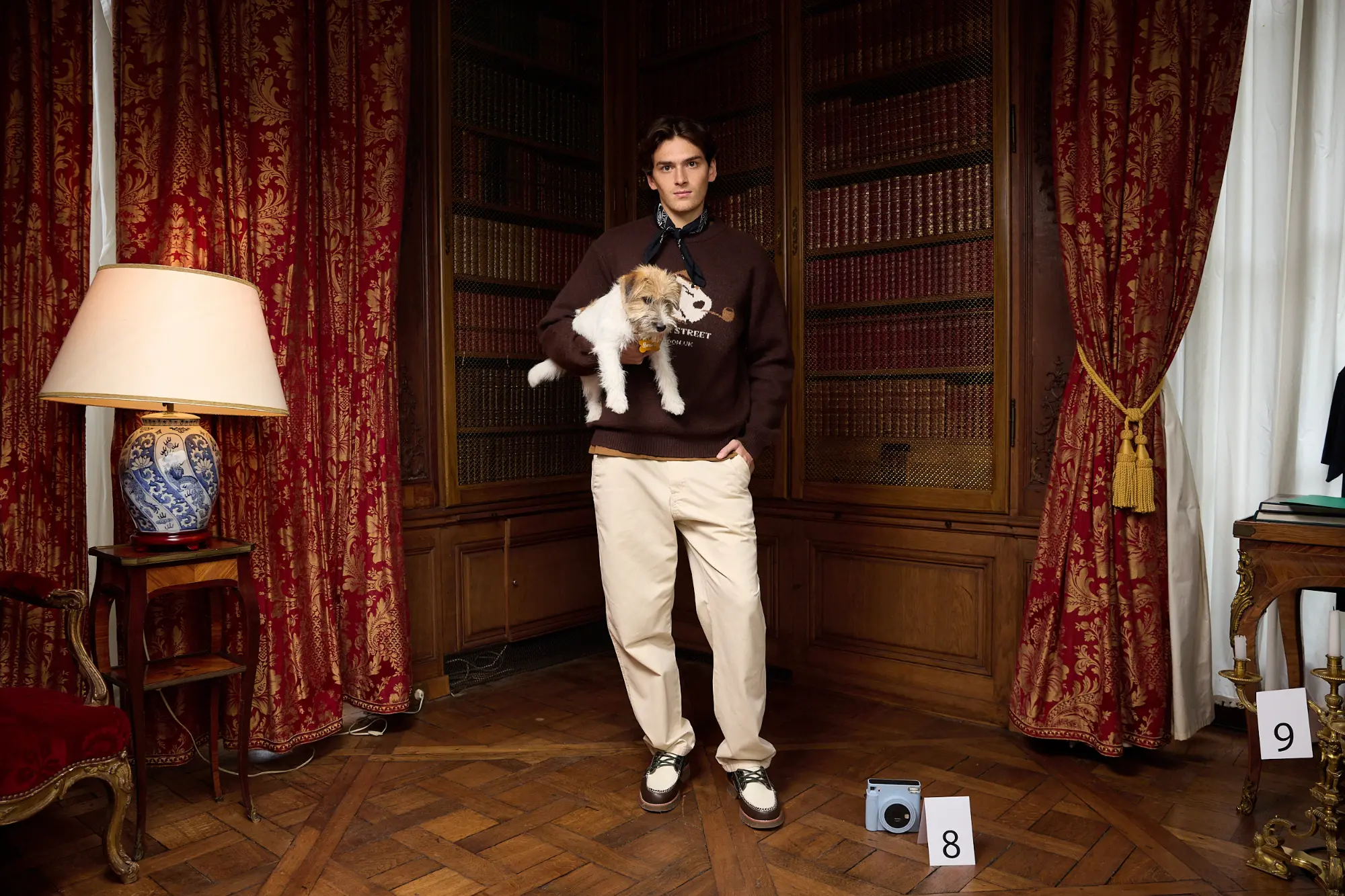 Pull col rond jacquard porté avec un pantalon jogger relaxed, un chien dans les bras, dans une bibliothèque ancienne