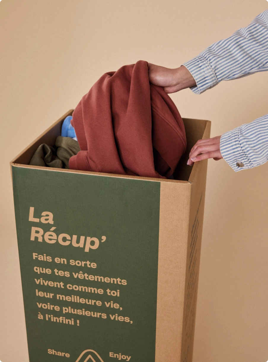 Une main dépose un sweat dans un bac de collecte de vêtements BZB
