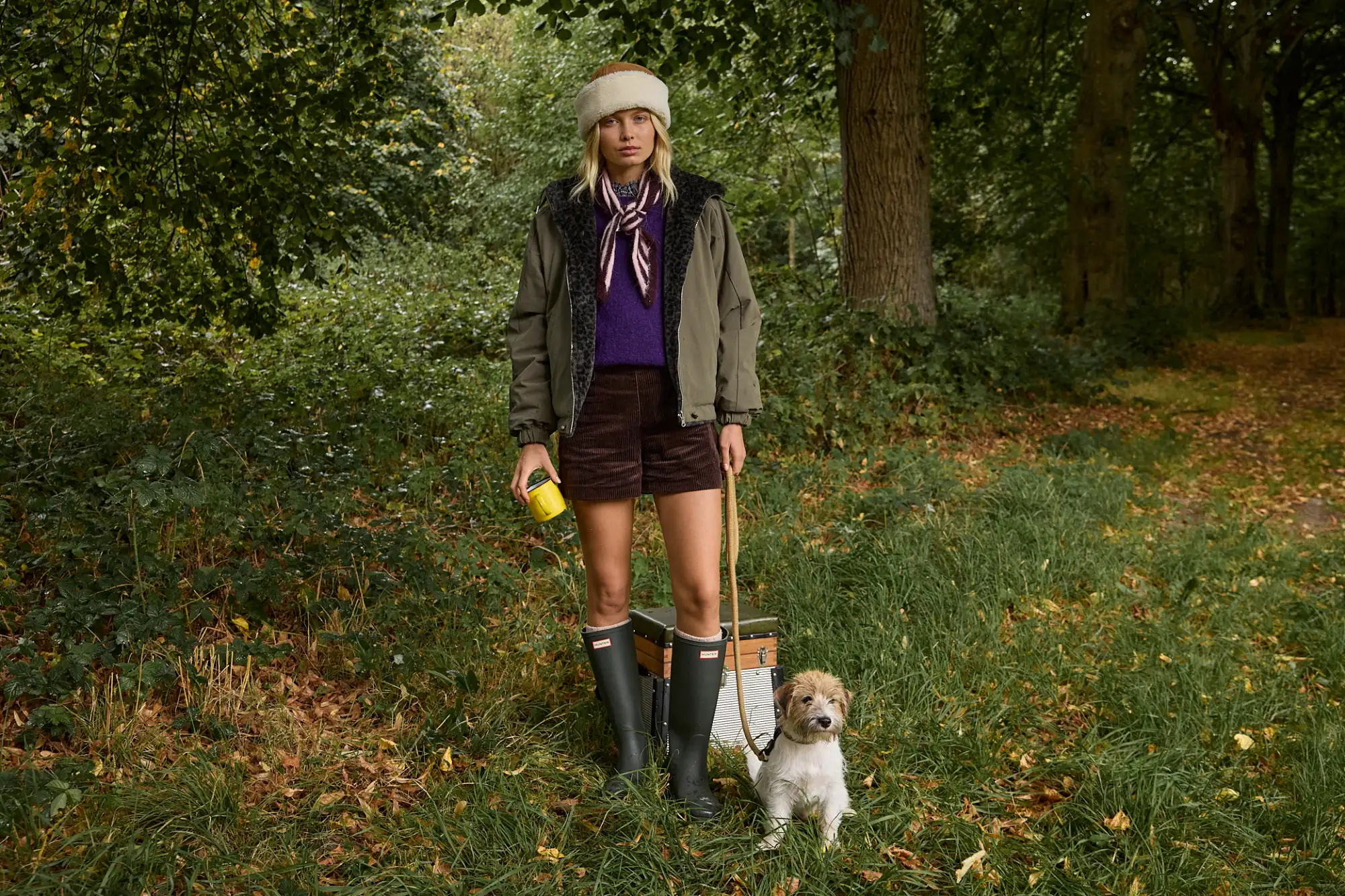 Parka réversible portée sur un pull sans manches et un short en velours, toque et écharpe rayée, en forêt avec un chien
