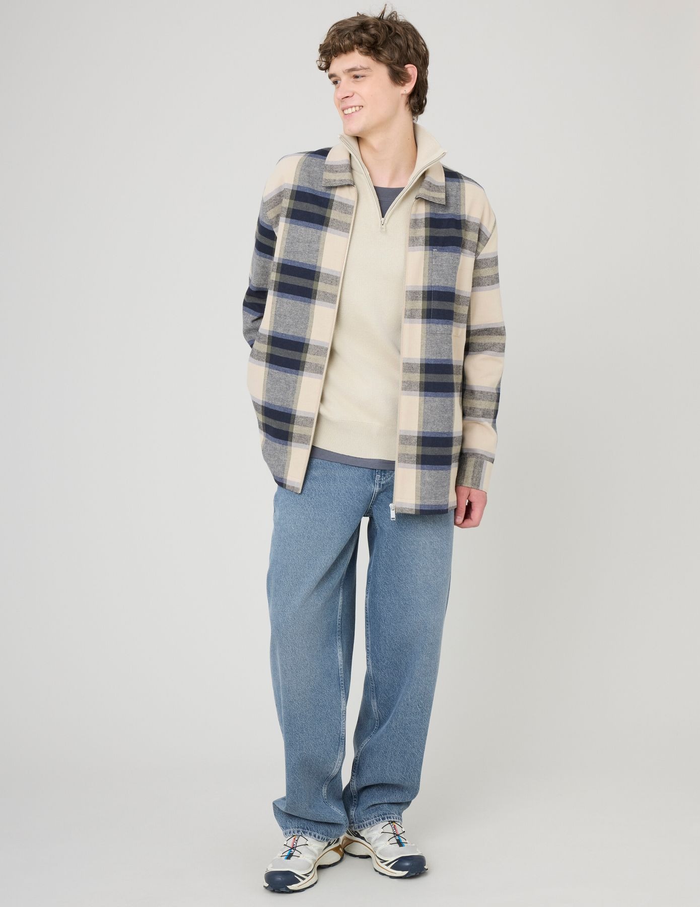 Look preppy chic avec pull noir à col zippé sous veste oversize à carreaux et pantalon clair